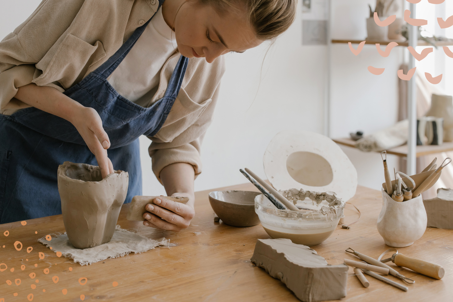 Junge Frau konzentriert beim Töpfern an einem Holztisch, umgeben von Werkzeugen und Ton – kreativer Moment in einem modernen Keramikstudio.