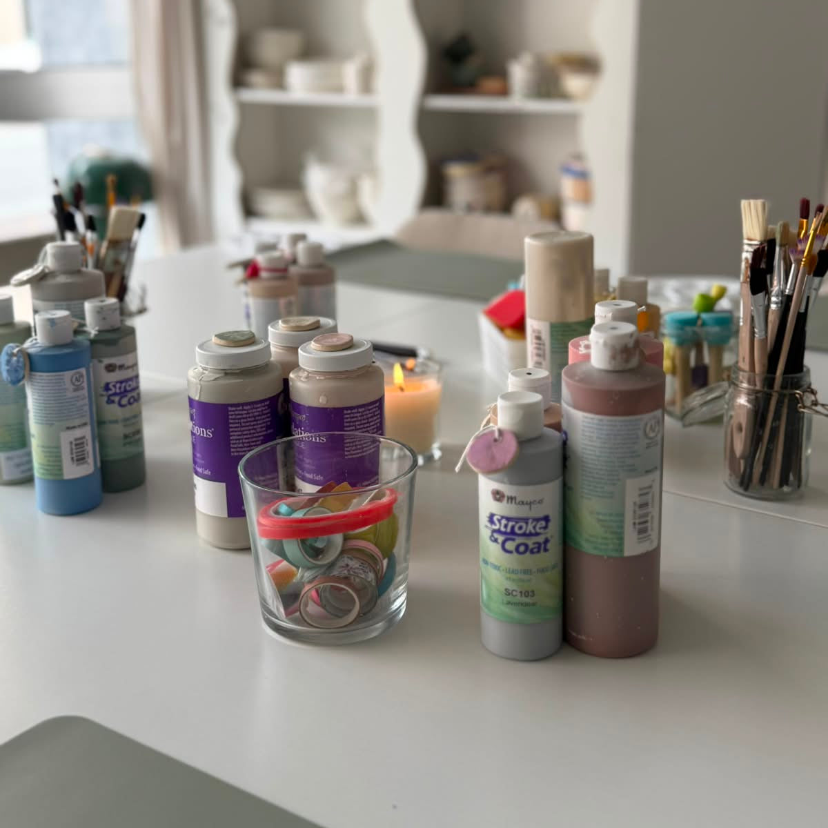 Mit Farben und Malutensilien gedeckter tisch in ruhiger, minimalistisch, grün-weißer Studioatmosphäre. 